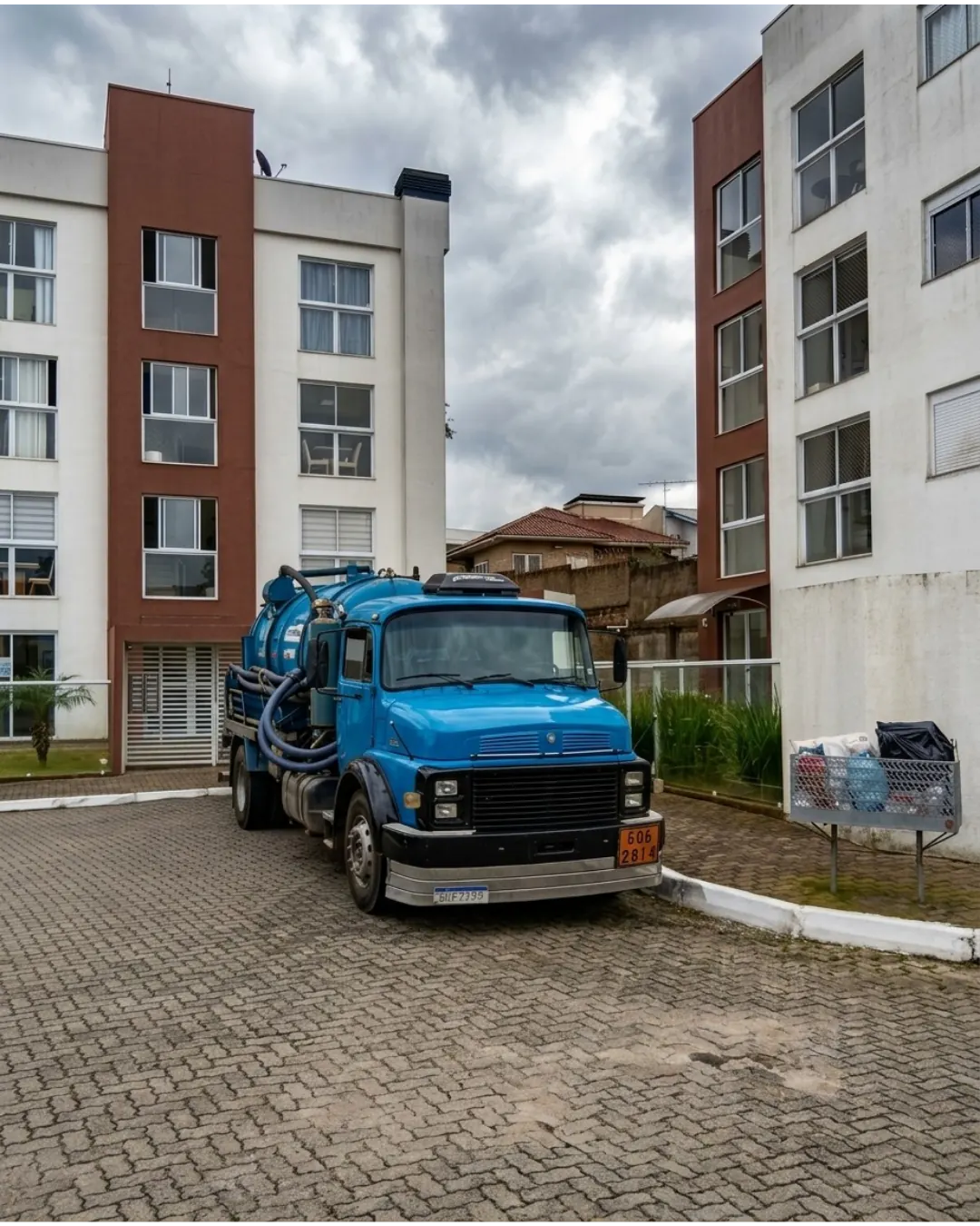 Caminhão auto vácuo azul posicionado entre edifícios residenciais